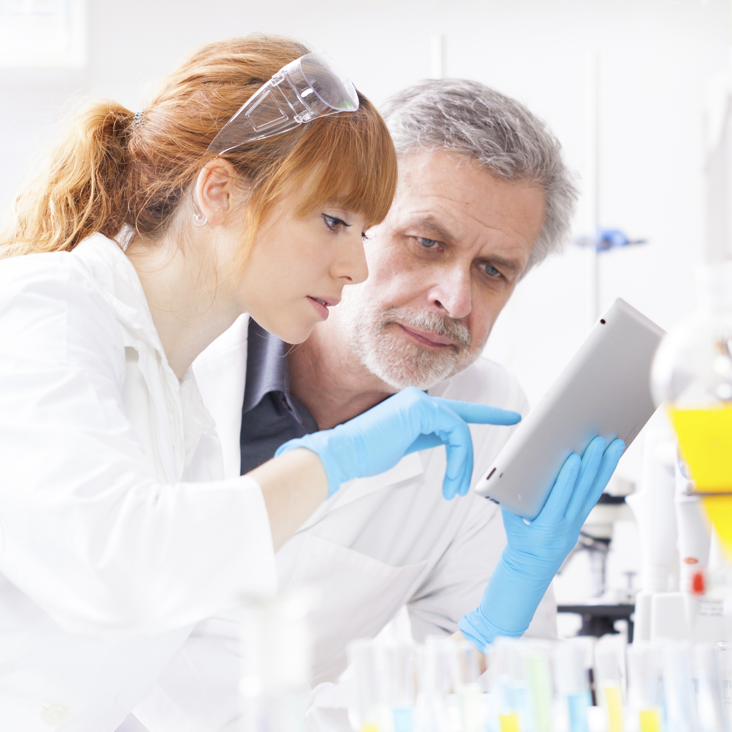 Two scientists discussing data on a tablet in a lab.