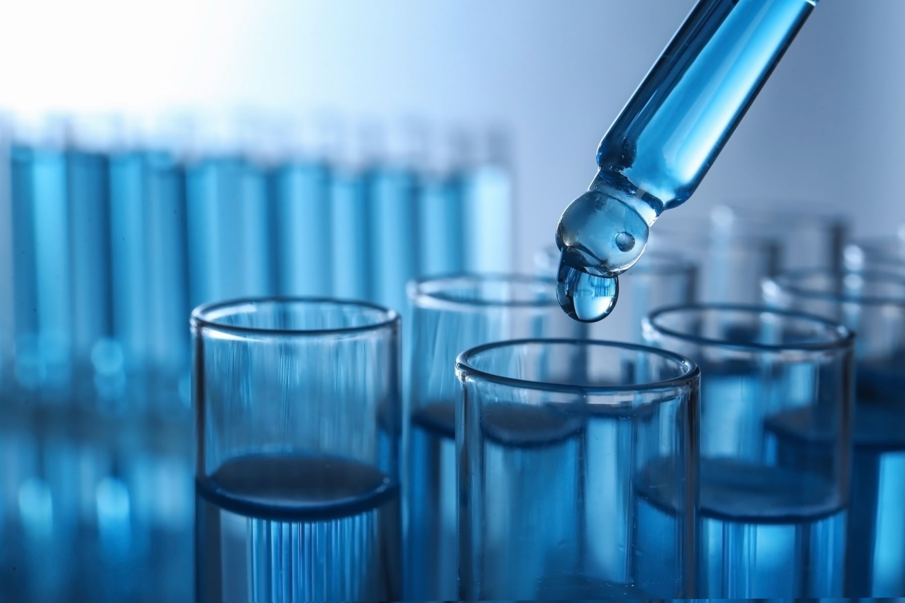 Pipette with liquid over test tubes in laboratory.