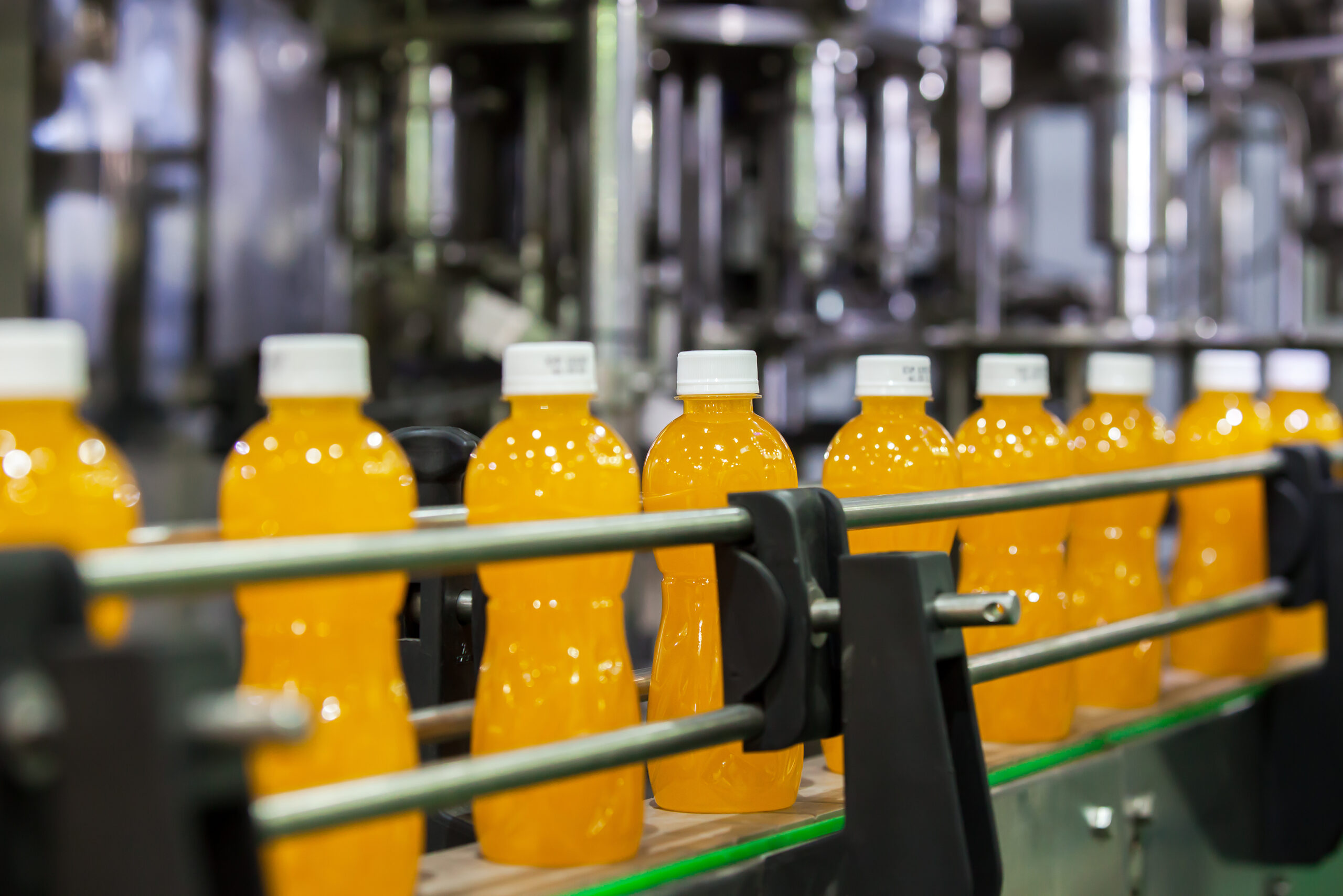 PackSafe Compliance Standard for packed beverage. Bottles lined up in a manufacturing line.
